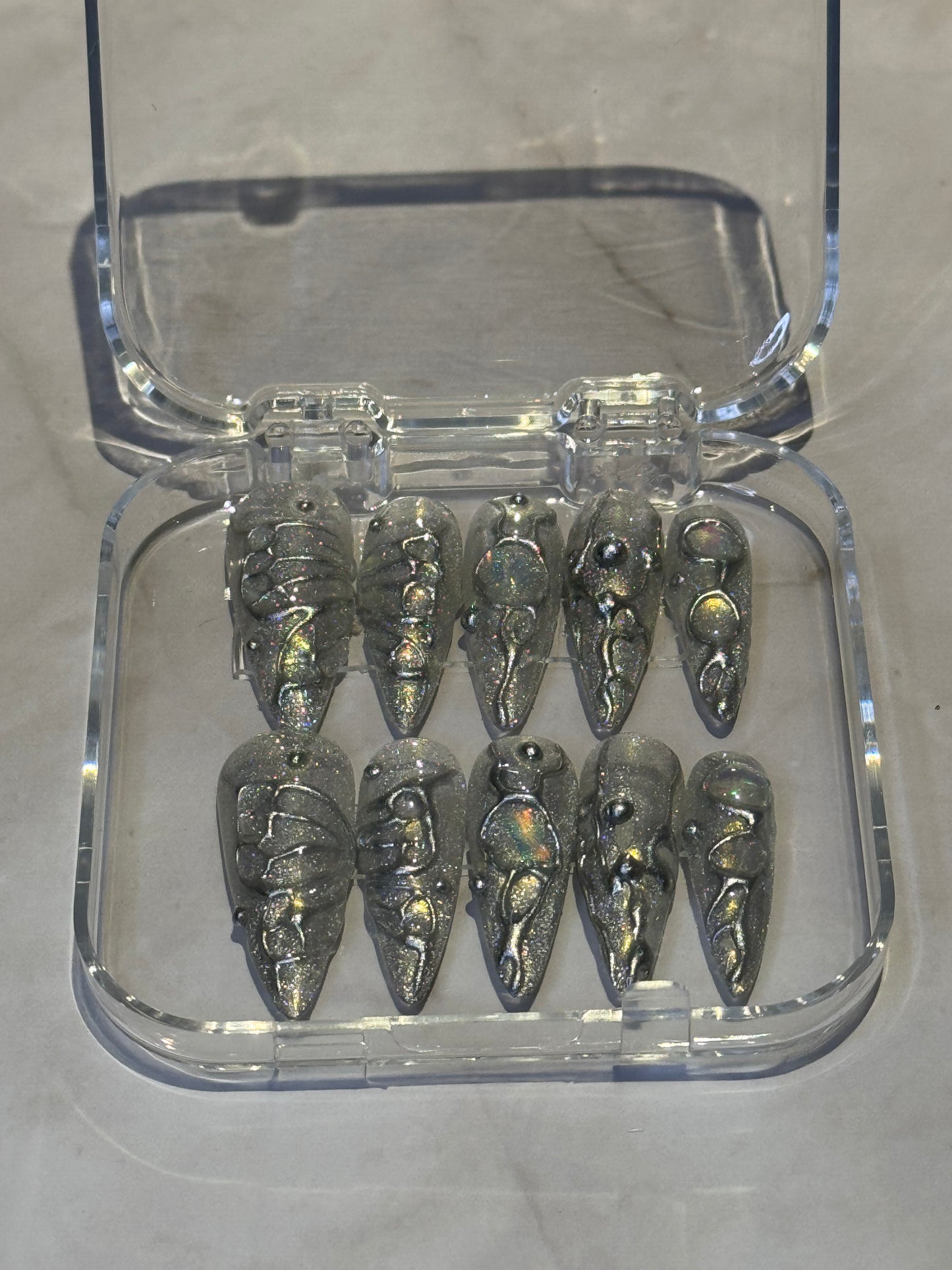 A collection of nail art designs displayed in a clear case, featuring a variety of patterns in grey and silver. lot of 3d effects,butterfly and rhinestones.
