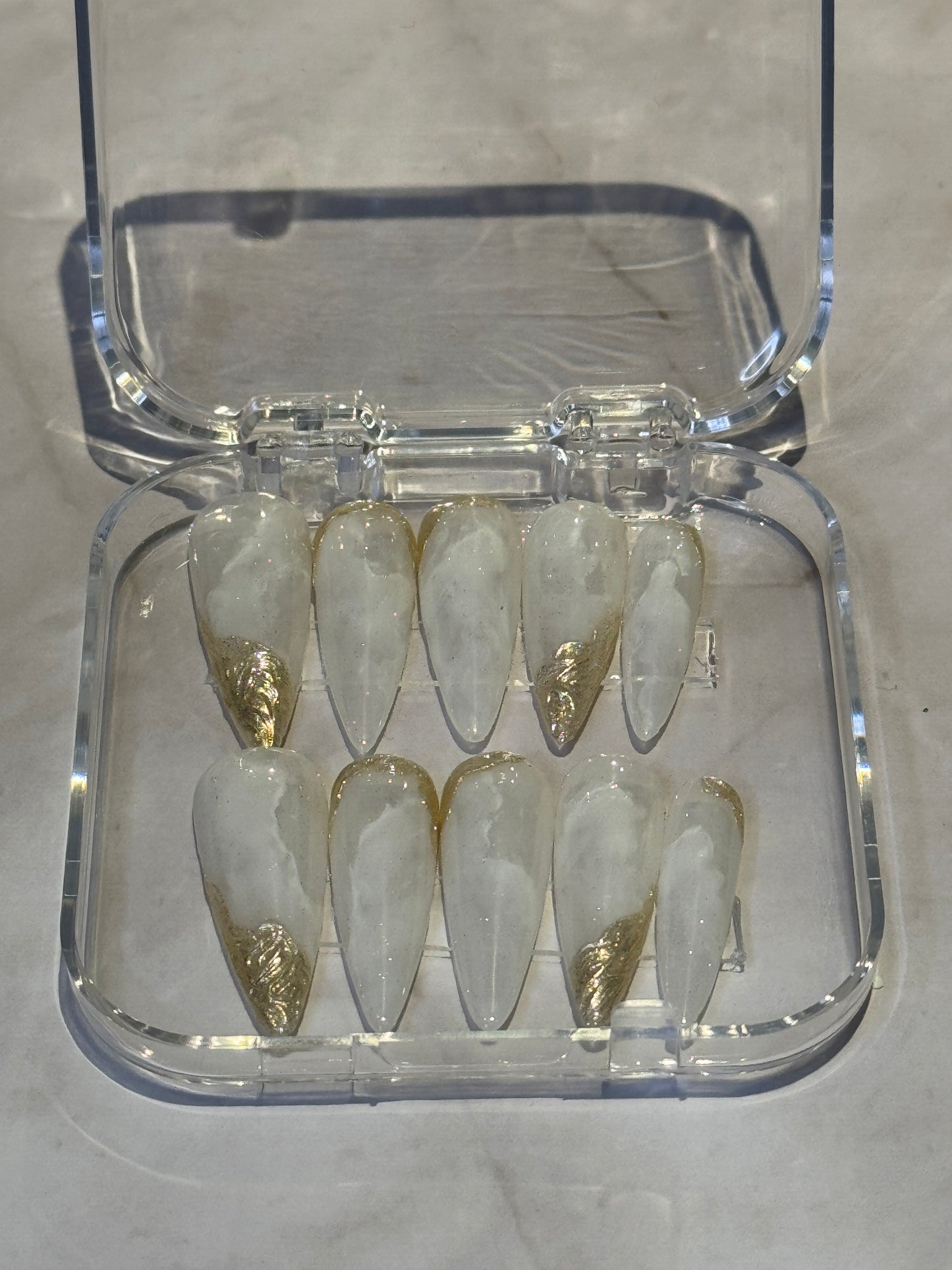Stiletto long nails with beautiful hand-painted marbled design in white tones. Finished with luxurious gold effects for an elegant, goddess-like appearance. Perfect for making a bold statement with premium nail art.