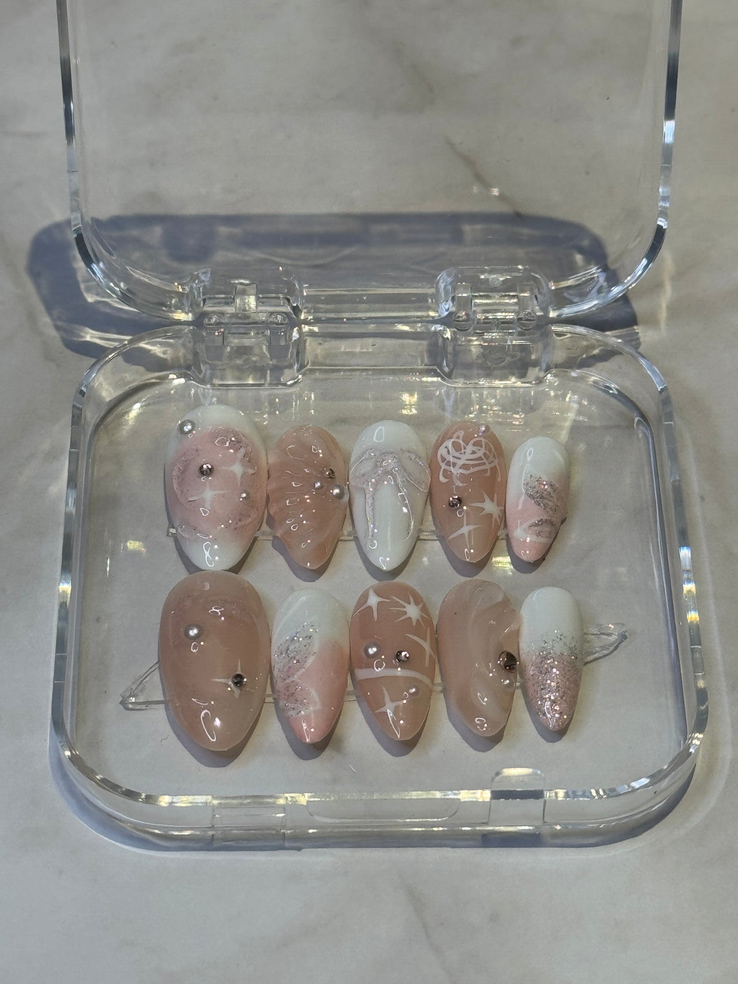 Medium almond press-on nails featuring hand-painted 3D details and rhinestone embellishments in nude pink and white. Each set includes three nails for a stunning, dimensional look. Perfect for adding elegance and sparkle to your manicure.