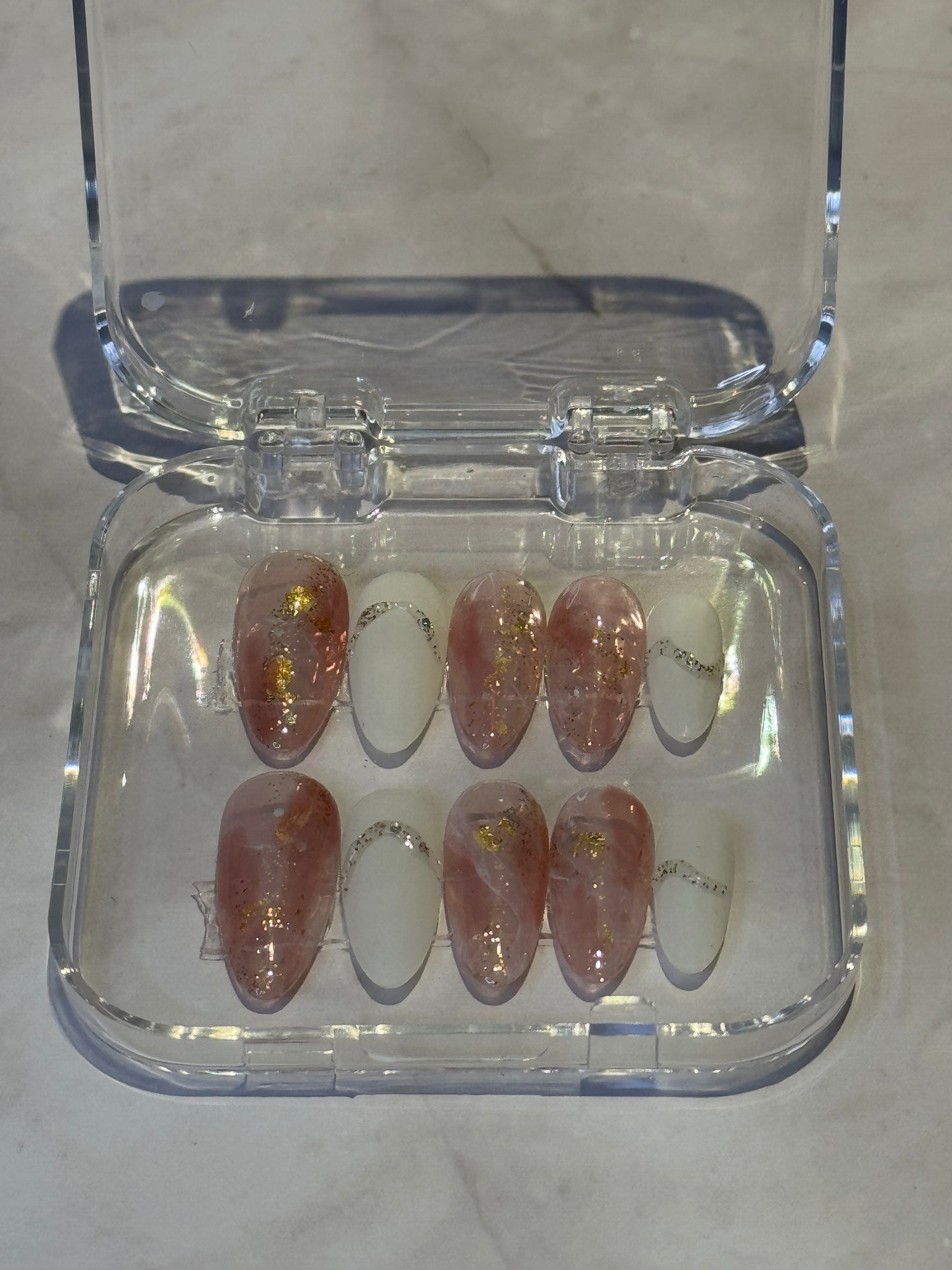 Medium almond nails with striking white and marmoreal pink tones and luxe gold accents. These stunning press-on nails combine elegant design with effortless application