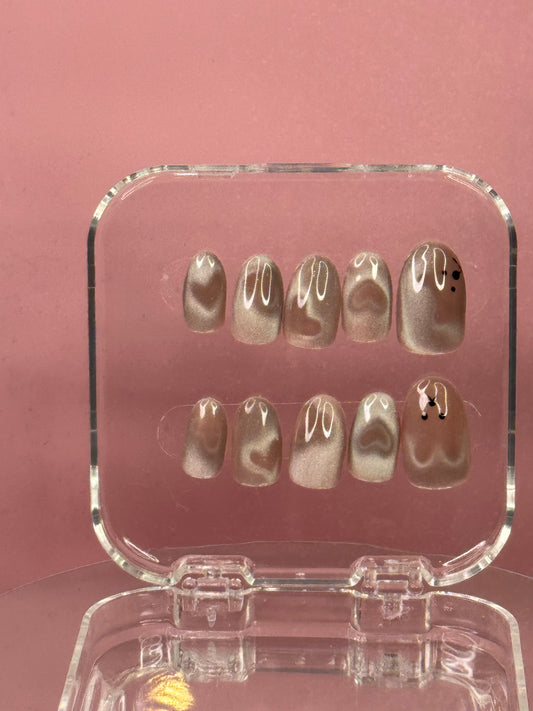 Press on nails with medium round tip with nude pink cat eye gel polish. Features mesmerizing cat eye effect with heart and teddy bear embellishments. Perfect for a playful, glamorous look that catches the light beautifully.