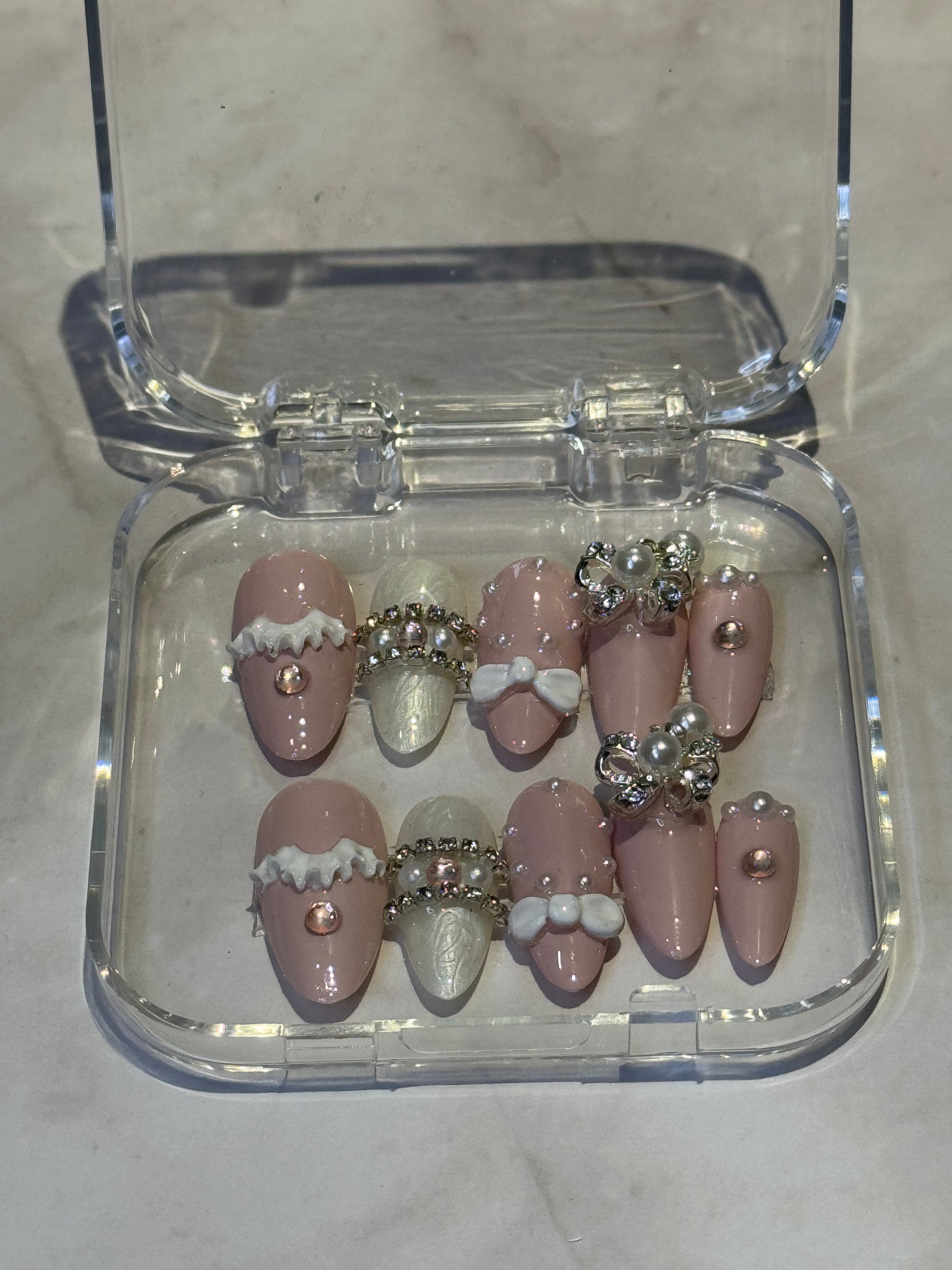 Almond medium press-on nails with a sweet and feminine design. Handcrafted with decorative rhinestones, pearls, and adorable hanging charms for that perfect finishing touch