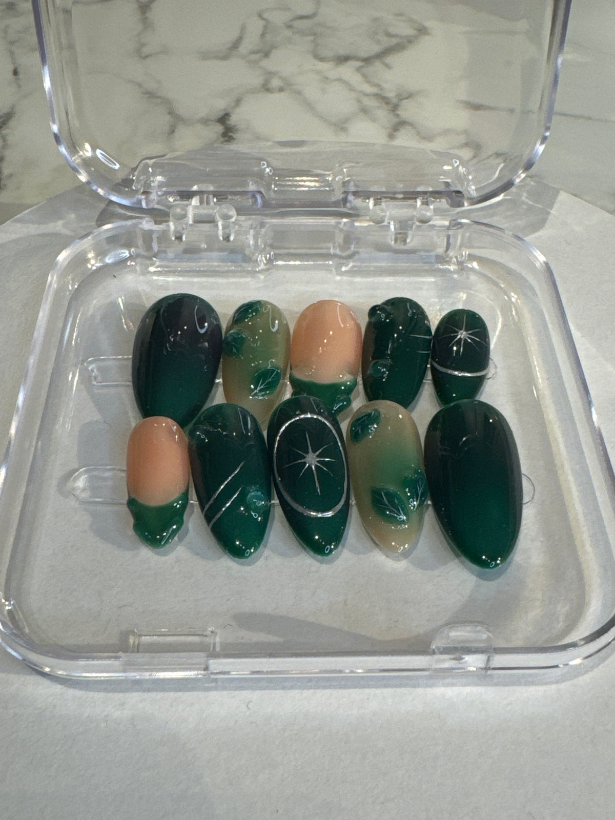 Nadine's Garden nails feature a stunning green almond shape with medium length. These luxe press-ons showcase intricate 3D details and elegant silver accents, finished with a classic French tip for a sophisticated, salon-quality look.