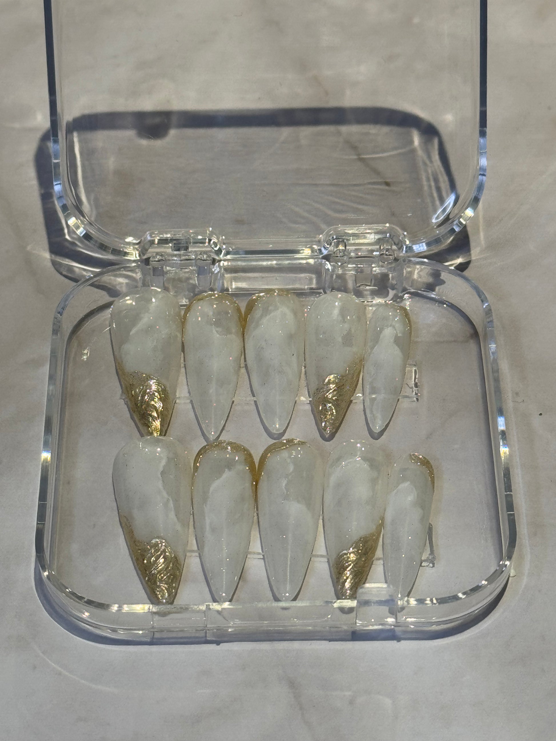 Stiletto long nails with beautiful hand-painted marbled design in white tones. Finished with luxurious gold effects for an elegant, goddess-like appearance. Perfect for making a bold statement with premium nail art.
