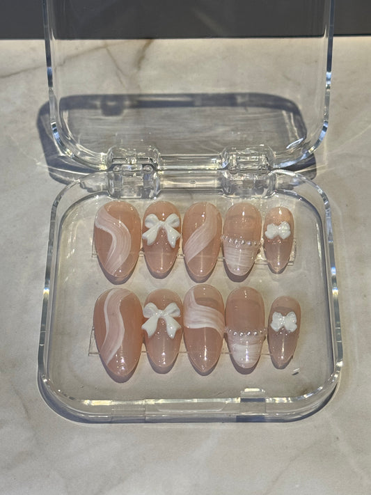 edium almond-shaped press-on nails in soft nude tones with delicate brushstroke detailing and charming bow and pearl embellishments. Each nail features hand-painted artistic strokes that add dimension and sophistication to your manicure. The combination of subtle nude shades with decorative accents creates a natural yet elegant look that complements any style, from everyday wear to special occasions.