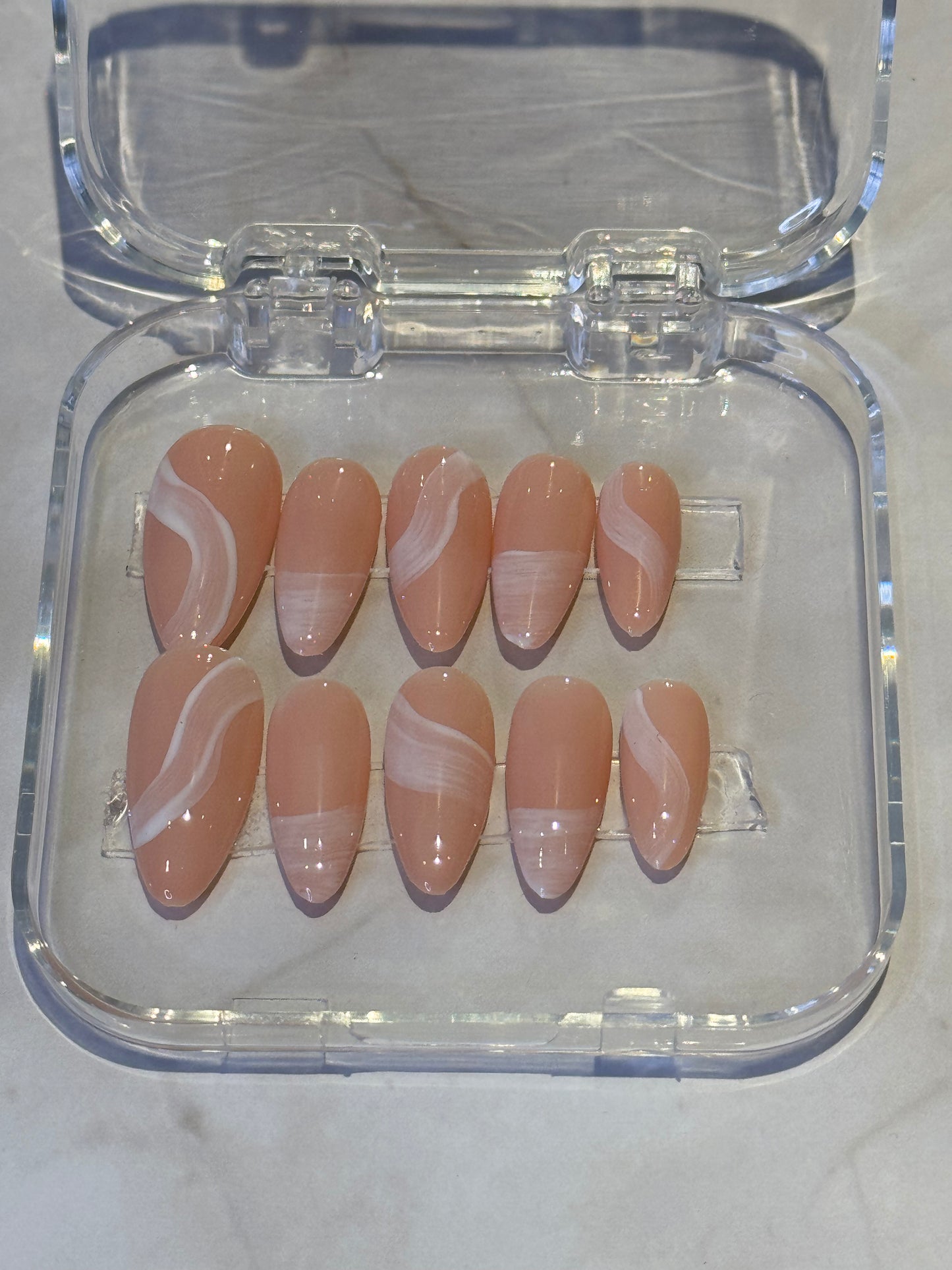 Medium almond-shaped press-on nails in soft nude tones, adorned with delicate brushstroke detailing. Each nail features hand-painted artistic strokes that add dimension and sophistication to your manicure. Perfect for a natural, elegant look that complements any style.&nbsp;