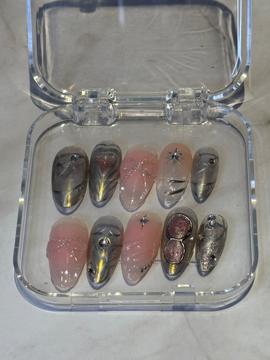 Medium almond shape with intricate details crafted for a bold, regal look. Features rhinestone embellishments, eye-detailed silver accents, and dark silver 3D effects for dimension. Soft pink ombre fades into gel details—all handmade for a unique warrior-inspired nail design that stands out. løsnegler